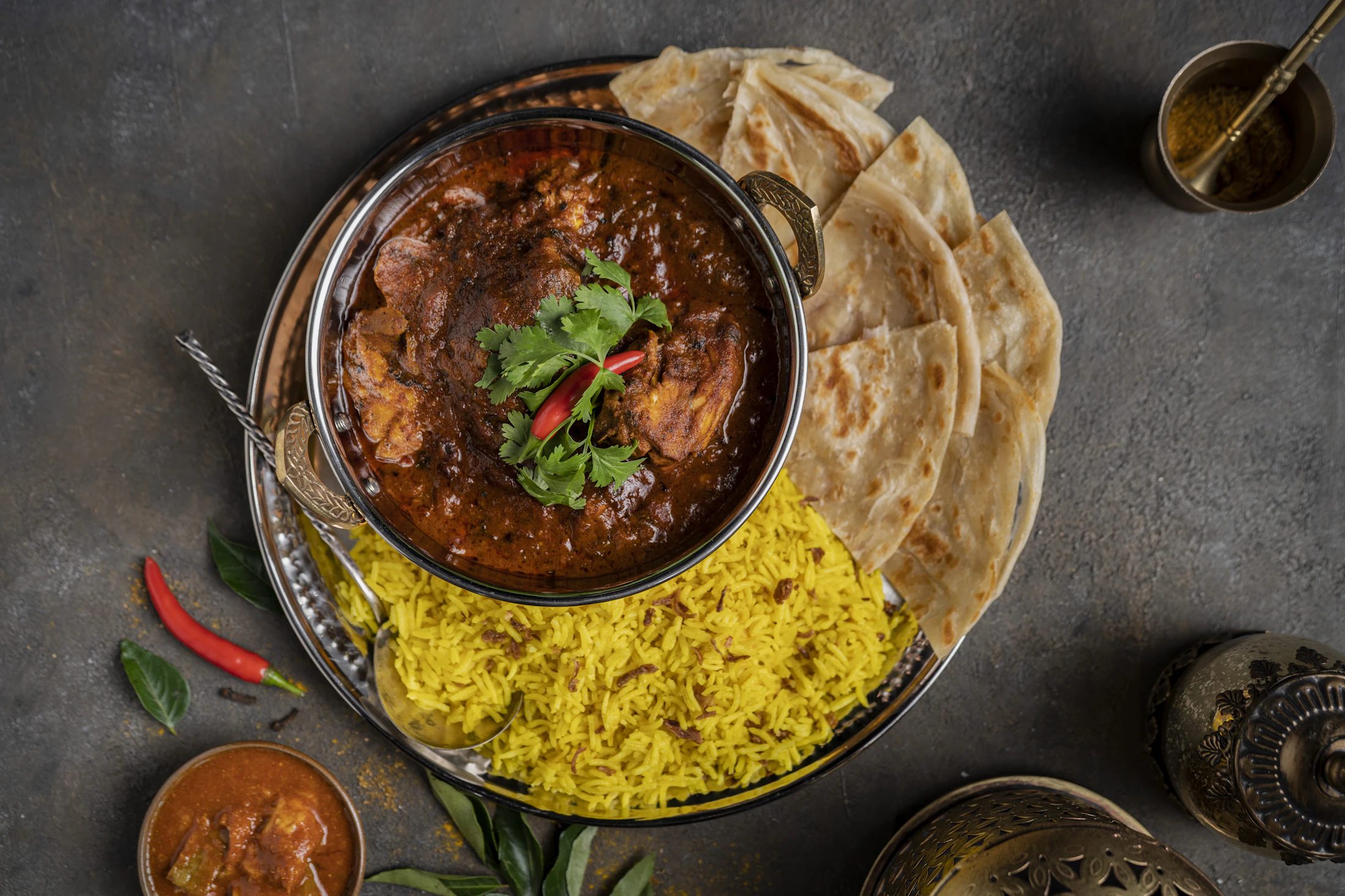 A bowl of spiced meat served with bread and rice