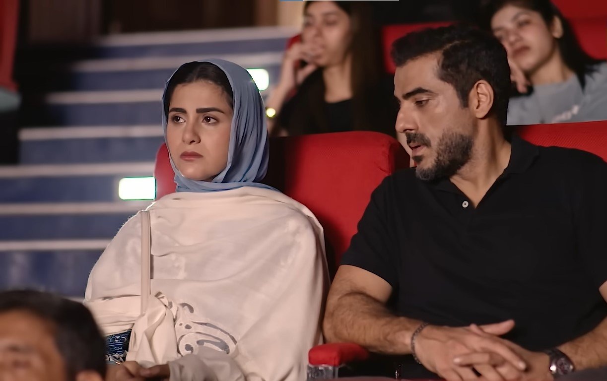Shabana seated beside a man in black in an auditorium